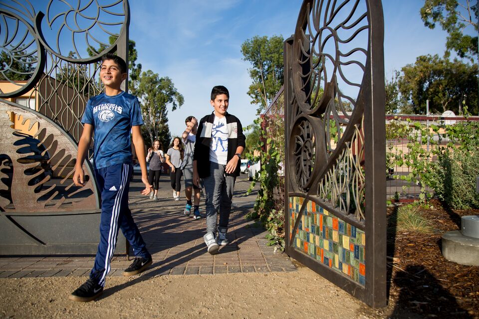 Two children walk through a decorative iron gateway to a city park