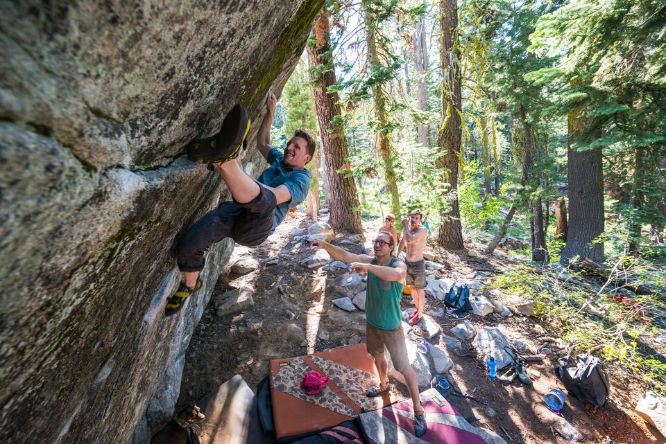 A climber ascends a boulder in a forest clearing