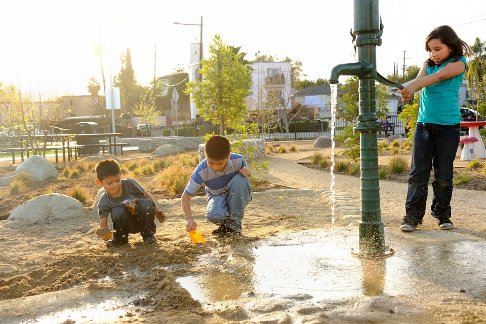 Three kids play at a water pump in a park